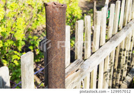 Old rusty metal pipe, pillar, and wooden fence at the garden in spring, summer 129957012