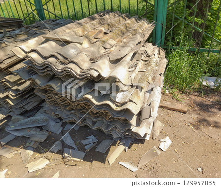 Old gray slate, stacked in uneven piles and broken into pieces of different shapes and sizes. Construction waste after roof repair Old gray slate, stacked in uneven piles and broken into pieces of different shapes and sizes. Construction waste after roof repair 129957035