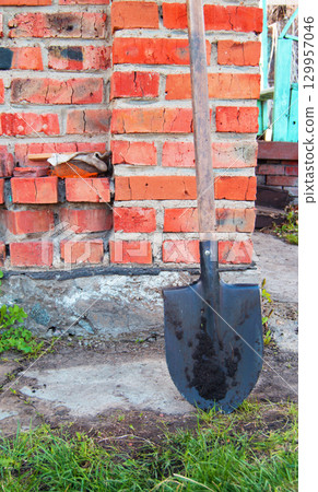 Metal shovel with wooden handle is a brick wall of the rural house 129957046