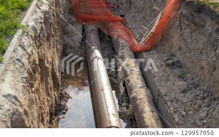 Close-up, repair of a heating main, laying of large-diameter metal pipes in a trench, protective warning signs 129957058