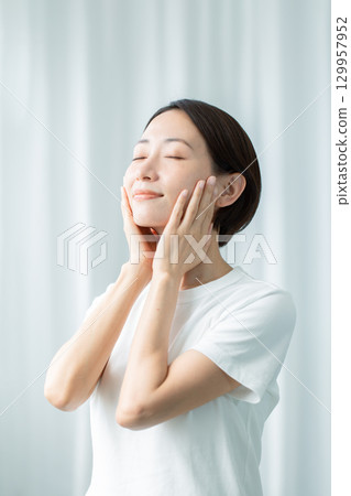 一位半透明的女人用雙手撫摸自己的臉頰，閉上眼睛感受濕氣滲透到她的上半身 129957952