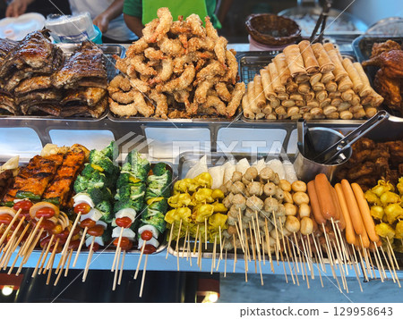 Colorful display of Thai street food with skewers, fried shrimp and spring rolls. Concept of culture, variety, community, tradition, flavor and lifestyle. Colorful display of Thai street food with skewers, fried shrimp and spring rolls. Concept of culture, variety, community, tradition, flavor and lifestyle. 129958643