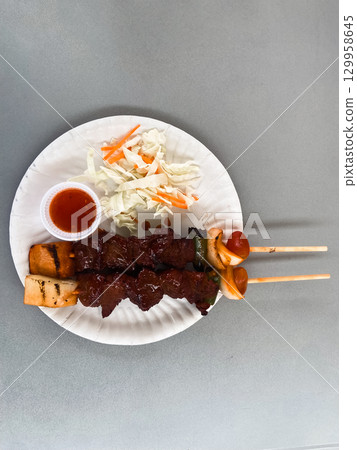Grilled beef skewers with vegetables and sauce served as Thai street food. Concept of culture, flavor, nutrition, community, tradition and lifestyle. Grilled beef skewers with vegetables and sauce served as Thai street food. Concept of culture, flavor, nutrition, community, tradition and lifestyle. 129958645