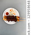 Thai street food beef skewers with vegetables and sauce on paper plate. Concept of tradition, culture, taste, nutrition, simplicity and community. 129958648