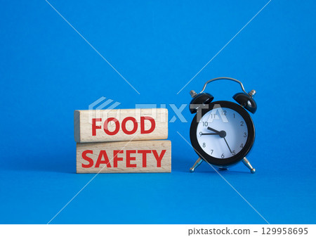 Food Safety symbol. Concept word Food Safety on wooden blocks. Beautiful blue background with alarm clock. Business and Food Safety concept. Copy space Food Safety symbol. Concept word Food Safety on wooden blocks. Beautiful blue background with alarm clock. Business and Food Safety concept. Copy space 129958695