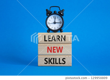 Learn new skills symbol. Concept words Learn new skills on wooden blocks. Beautiful blue background with alarm clock. Business and Learn new skills concept. Copy space. 129958809