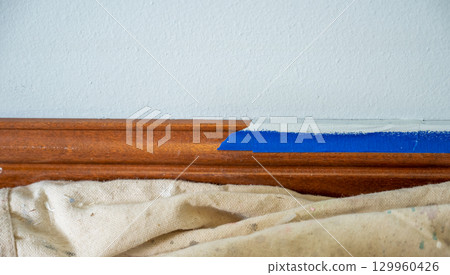 Interior painting project in a home with careful taping along the wooden trim in a light and airy room 129960426