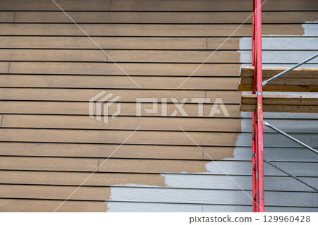 House exterior renovation project with scaffolding and partially painted walls in progress during daylight hours 129960428