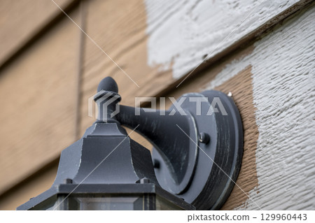 Wall-mounted outdoor light fixture being painted on a weathered wooden surface in daylight 129960443