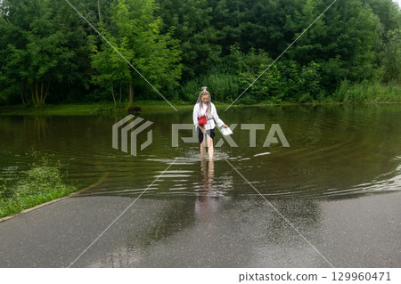 woman walks barefoot through a deep puddle in a flooded park on a rainy day 129960471