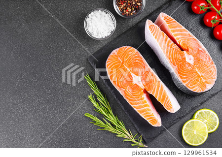 Fresh raw salmon or trout steaks with tomatoes, spices, rosemary and lime on black stone background 129961534