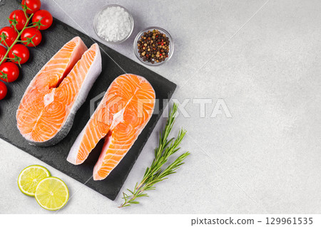 Two fresh raw salmon steaks with tomatoes, spices, rosemary and lime on white stone background Two fresh raw salmon steaks with tomatoes, spices, rosemary and lime on white stone background 129961535