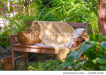 Wooden garden bench with yellow blanket and straw basket, place fo relax in cozy summer backyard Wooden garden bench with yellow blanket and straw basket, place fo relax in cozy summer backyard 129961548