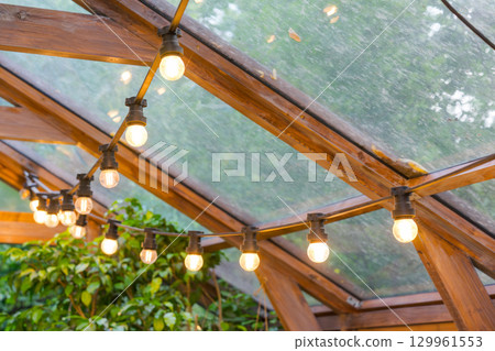 Rustic garland with lamp blulb lanterns glowing under of wooden celling, home decor, illumination 129961553