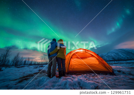 A couple is standing in front of a tent in the snow A couple is standing in front of a tent in the snow 129961731