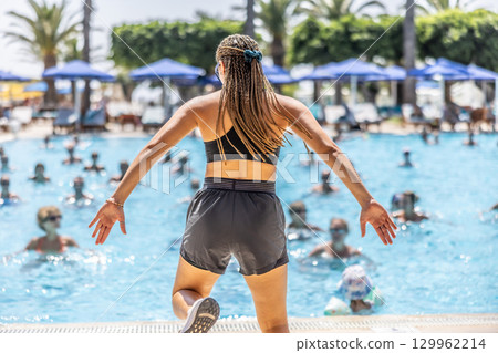 A young female Sports Animator is doing water aerobics for people in the pool of a hotel resort 129962214