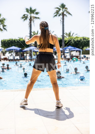 A young female Sports Animator is doing water aerobics for people in the pool of a hotel resort A young female Sports Animator is doing water aerobics for people in the pool of a hotel resort 129962215
