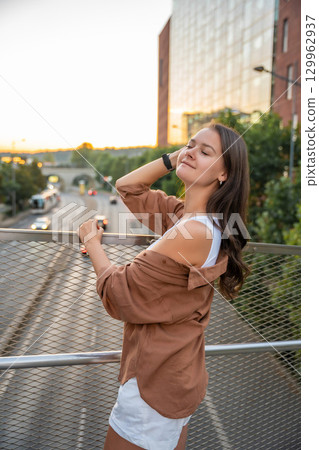 Attractive young woman enjoying her free time at sunset outdoor. Happy girl portrait at summer. Freedom lifestyle summer concept. Sun glow on background. Attractive young woman enjoying her free time at sunset outdoor. Happy girl portrait at summer. Freedom lifestyle summer concept. Sun glow on background. 129962937