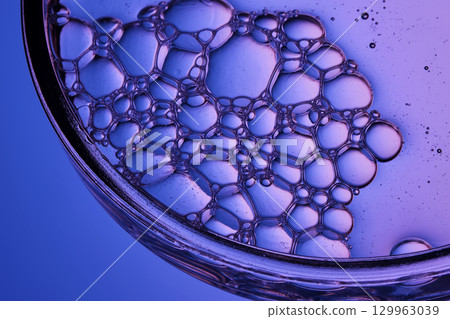 Serum with bubbles in a petri dish on a purple background. 129963039