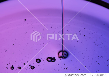 Serum or body cream flows into a petri dish on a purple background. Serum or body cream flows into a petri dish on a purple background. 129963058
