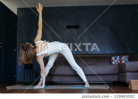 woman standing in Wide Legged Forward Bend Twist yoga pose at home 129963082