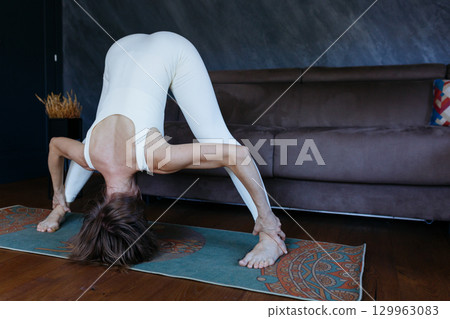 woman standing in Wide Legged Forward Bend yoga pose at home 129963083