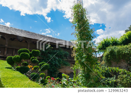 Beautiful green garden with trees; flowers and full summer bloom. Wood old gate and stone wall around the garden. Beautiful green garden with trees; flowers and full summer bloom. Wood old gate and stone wall around the garden. 129963243