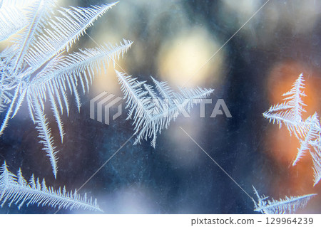 Frost patterns create intricate designs on a window during a cold winter morning Frost patterns create intricate designs on a window during a cold winter morning 129964239