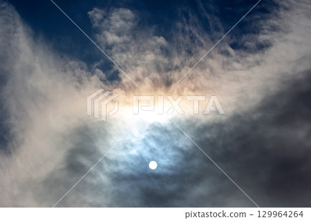 Colorful clouds surround bright sun during late afternoon in a clear sky 129964264