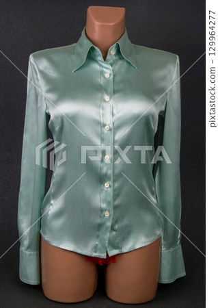 Elegant green satin blouse displayed on a mannequin against a dark background 129964277