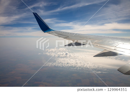 View of airplane wing flying above clouds and land under bright sky View of airplane wing flying above clouds and land under bright sky 129964351