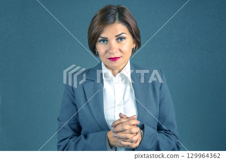 Confident professional woman in business attire poses against a blue backdrop 129964362