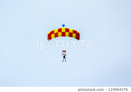Parachutist descends from the sky during an exciting aerial adventure over a clear horizon Parachutist descends from the sky during an exciting aerial adventure over a clear horizon 129964376