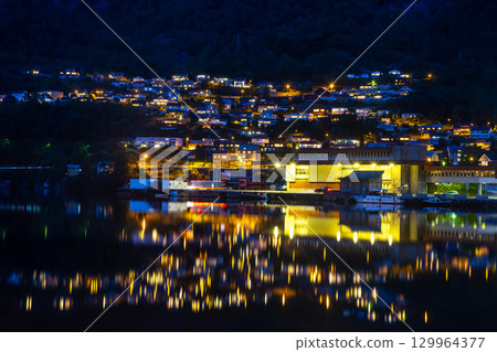 Nighttime view of a Norwegian town reflecting on the water at dusk Nighttime view of a Norwegian town reflecting on the water at dusk 129964377
