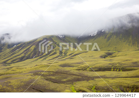 Explore the rugged beauty of Iceland's landscape with lush green hills and misty mountains 129964417