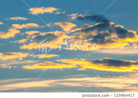 Vibrant sunset clouds illuminated by golden light in the evening sky above the horizon 129964427