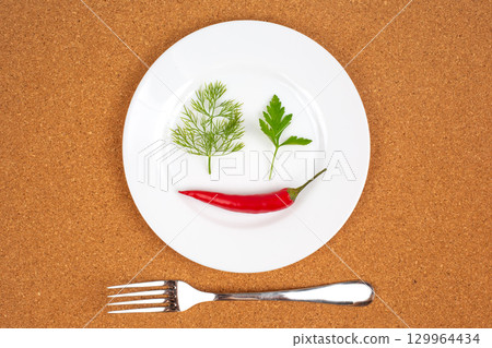 Chili pepper, cilantro, and dill arranged creatively on a white plate for artistic presentation 129964434