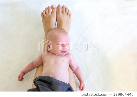 Baby resting peacefully on mother's legs in soft lighting during a calm afternoon at home 129964443