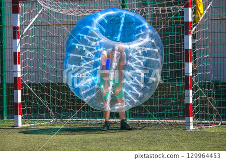 Person prepares to play bubble soccer in a sunny outdoor sports field 129964453