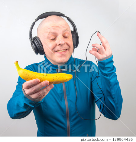 Man enjoying music with banana as a playful headset in studio setting 129964456