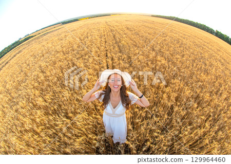 Woman in white dress enjoying summer in golden wheat field under sunny blue sky Woman in white dress enjoying summer in golden wheat field under sunny blue sky 129964460