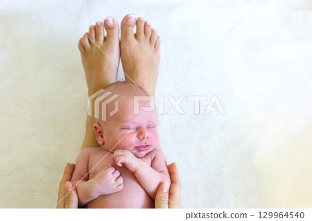 Newborn baby peacefully resting in hands with adult feet in view Newborn baby peacefully resting in hands with adult feet in view 129964540
