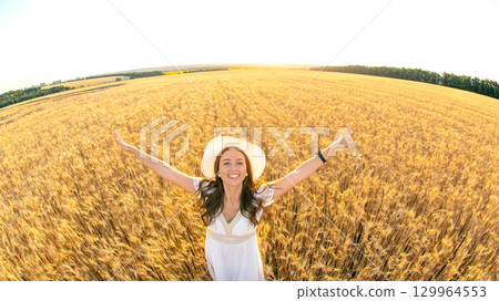 Woman enjoys sunny day in expansive golden wheat field with arms outstretched 129964553
