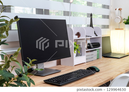 Modern and organized workspace with monitor, keyboard, laptop, shelving unit, and decorative items 129964630