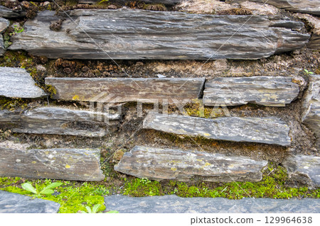 Gray structural stone wall of the ancient building consists of old dark bricks. Nature background. 129964638