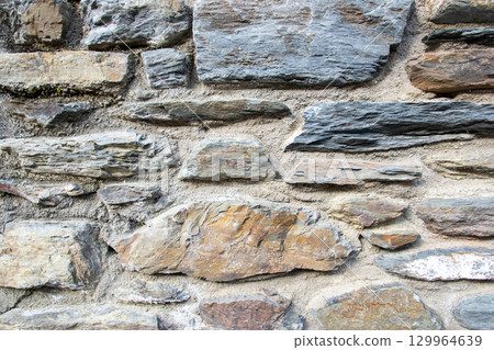 Gray structural stone wall of the ancient building consists of old dark bricks. Nature background. Gray structural stone wall of the ancient building consists of old dark bricks. Nature background. 129964639