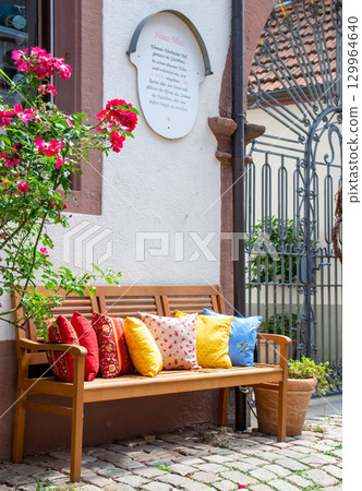 Wood romantic bench with a lot of multicolor pillows outdoor near stone house and rose. 129964640