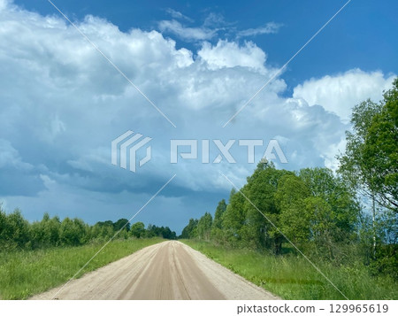 A Scenic Dusty Road Winding Its Way Through a Lush Green Landscape Beneath Dramatic Clouds A Scenic Dusty Road Winding Its Way Through a Lush Green Landscape Beneath Dramatic Clouds 129965619