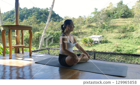 Woman in lotus pose on bamboo hut terrace enjoys calm and connection with tropical nature Woman in lotus pose on bamboo hut terrace enjoys calm and connection with tropical nature 129965858