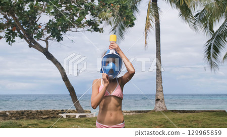 Girl gives a thumbs up after putting on snorkel mask surrounded by palm trees and tropical ocean view Girl gives a thumbs up after putting on snorkel mask surrounded by palm trees and tropical ocean view 129965859